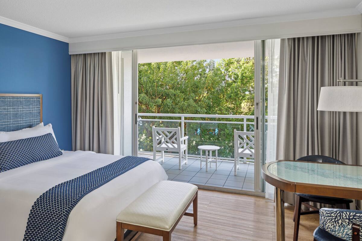 Ein Hotelzimmer mit einem großen Bett, einem Balkon mit Sitzgelegenheiten und einem Esstisch.