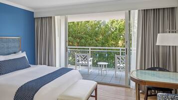 A hotel room with a large bed, a balcony with chairs, and a dining table.