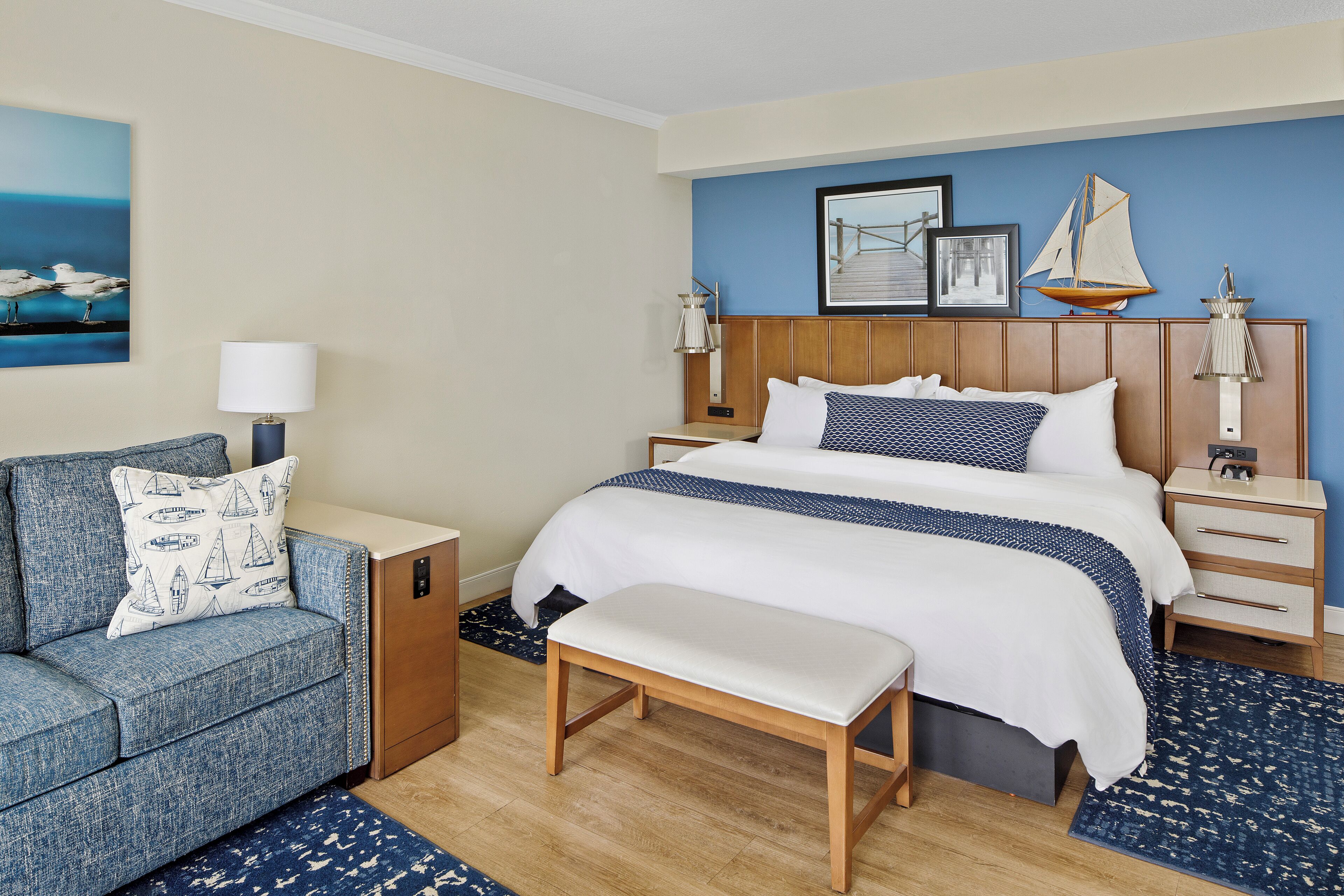 A hotel room with a bed, a bench, a nightstand, a lamp, and a sofa.