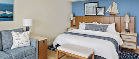A hotel room with a bed, a bench, a nightstand, a lamp, and a sofa.