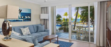 A hotel room with a balcony, a sofa, a coffee table, and a painting of seagulls.