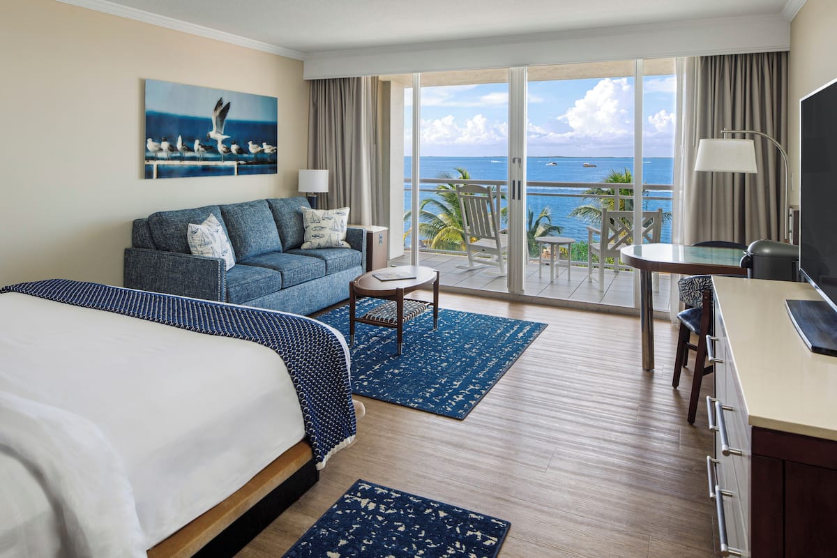 Ein Hotelzimmer mit Bett, einer Couch, einem Schreibtisch, einem Sessel und einem Balkon mit Meerblick.