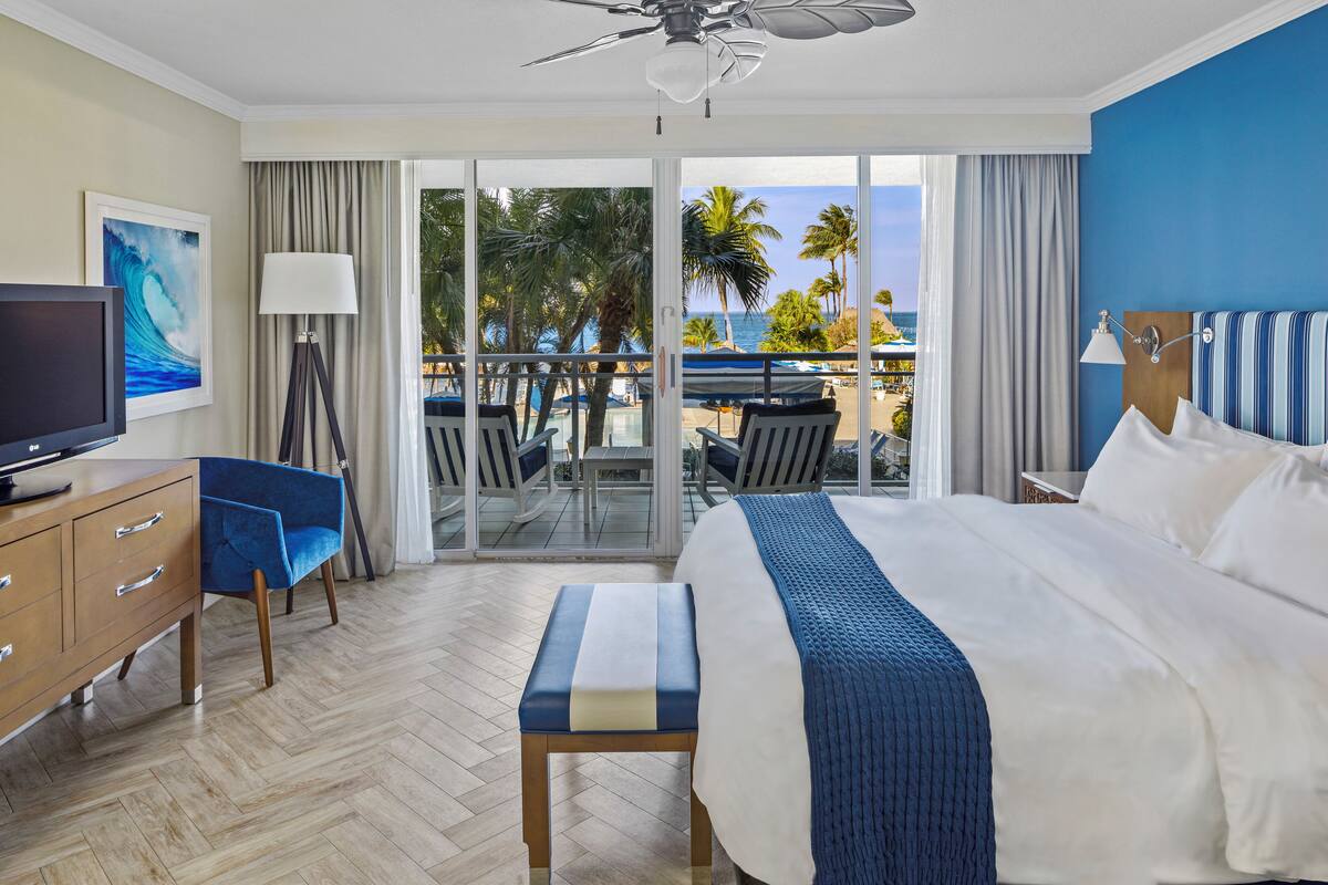 Ein Hotelzimmer mit Bett, Fernseher, Schreibtisch und Blick auf den Strand.