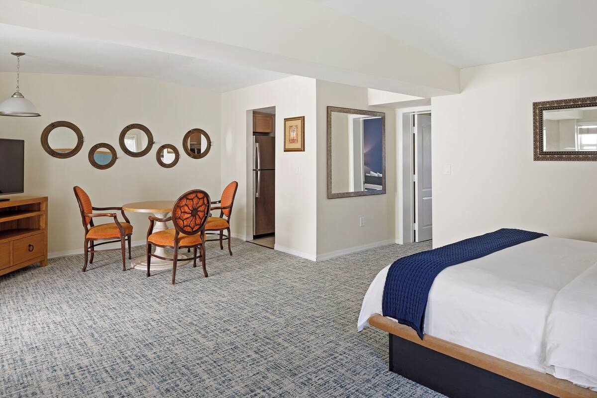 Ein Hotelzimmer mit einem Bett, einem Schreibtisch mit Stühlen, einem Kühlschrank und einem Fernseher.