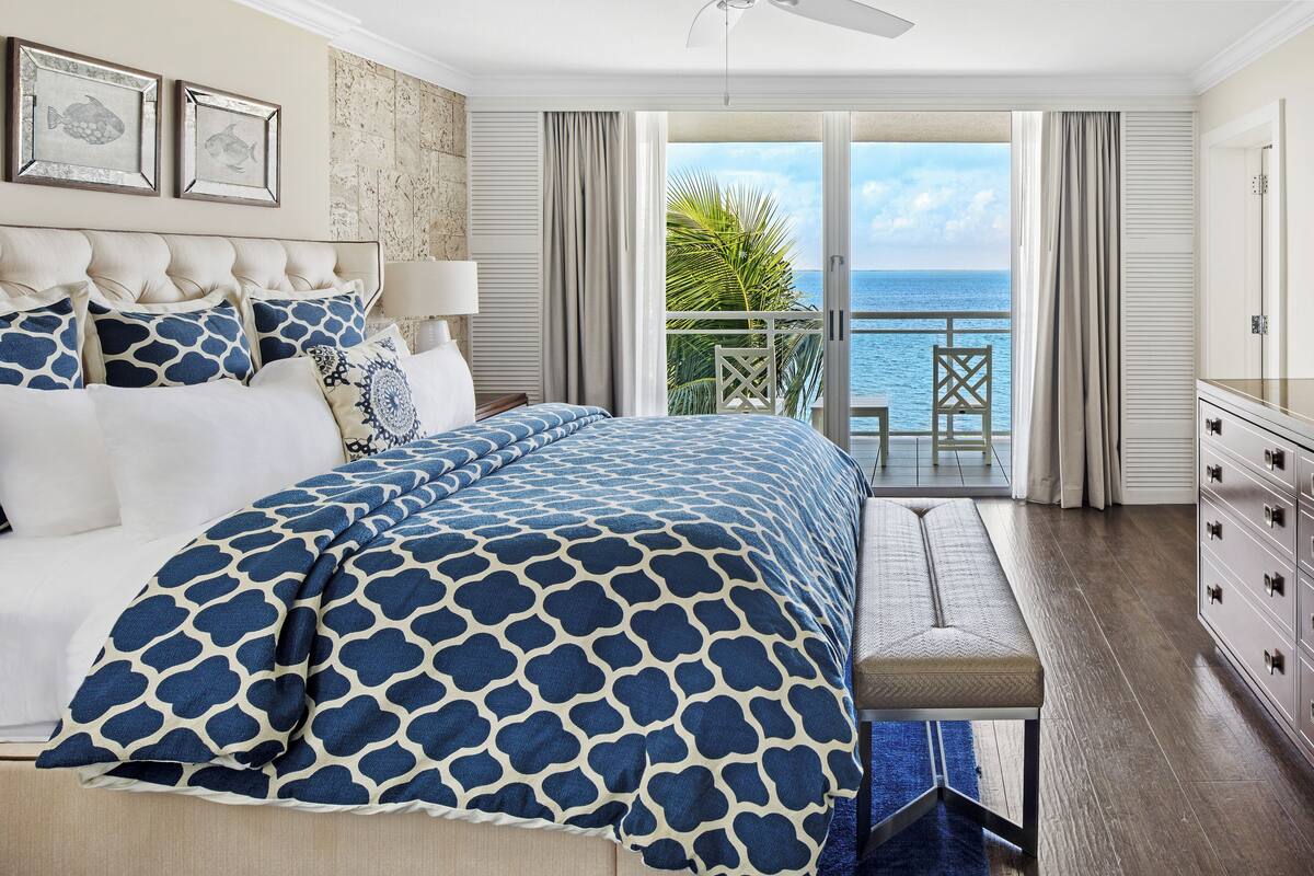 Ein Schlafzimmer mit einem großen Bett, einer Bank, einem Schminktisch und einem Balkon mit Meerblick.