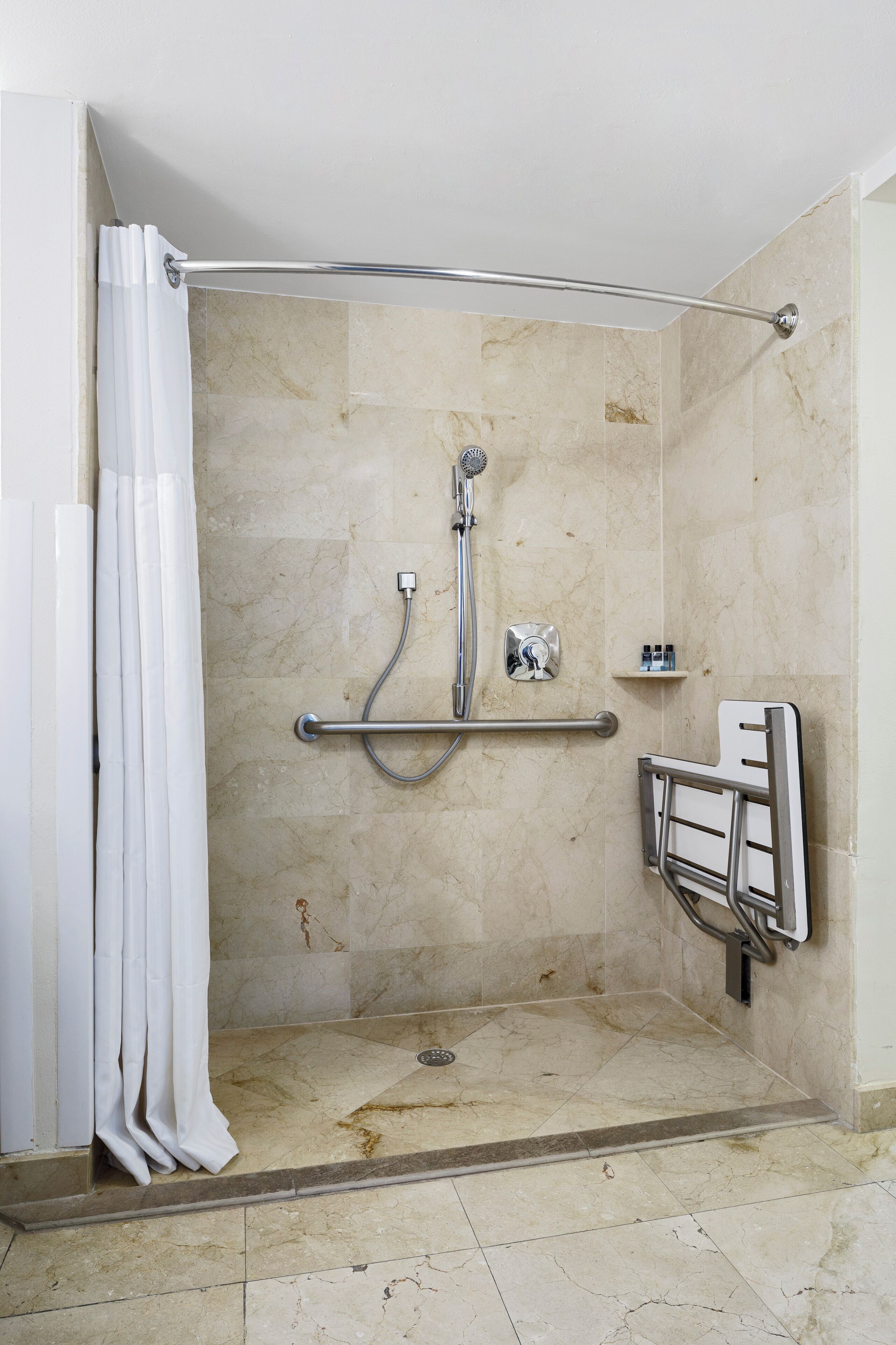 A shower area with a grab bar, a showerhead, and a shelf with toiletries.