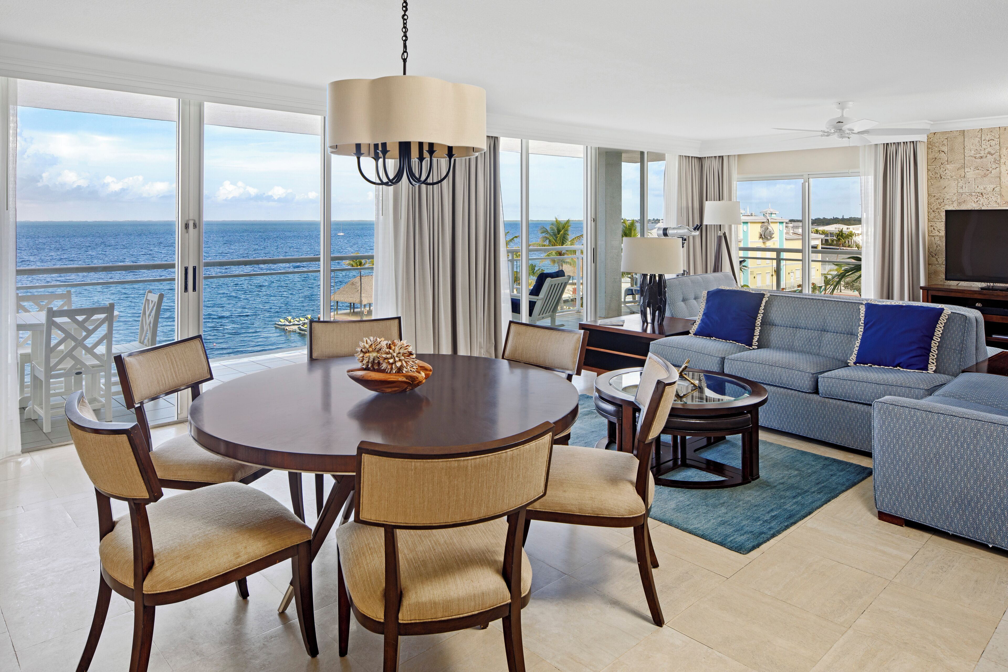 Ein geräumiges Wohnzimmer mit großem Fenster zum Meer, einem runden Esstisch mit Stühlen, einer Couch und einem Fernseher.