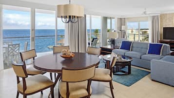 Ein geräumiges Wohnzimmer mit großem Fenster zum Meer, einem runden Esstisch mit Stühlen, einer Couch und einem Fernseher.