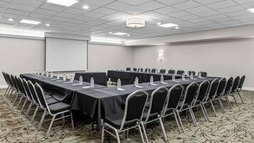 Un salón de conferencias con una larga mesa, sillas, botellas de agua y una pantalla para proyector.