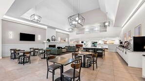 Un hall de hotel espacioso con varias zonas de estar, una cocina y un televisor de pantalla plana montado en la pared.