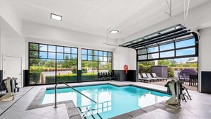 Una piscina interior moderna con paredes de vidrio transparente, suelo de baldosas y vistas al exterior.