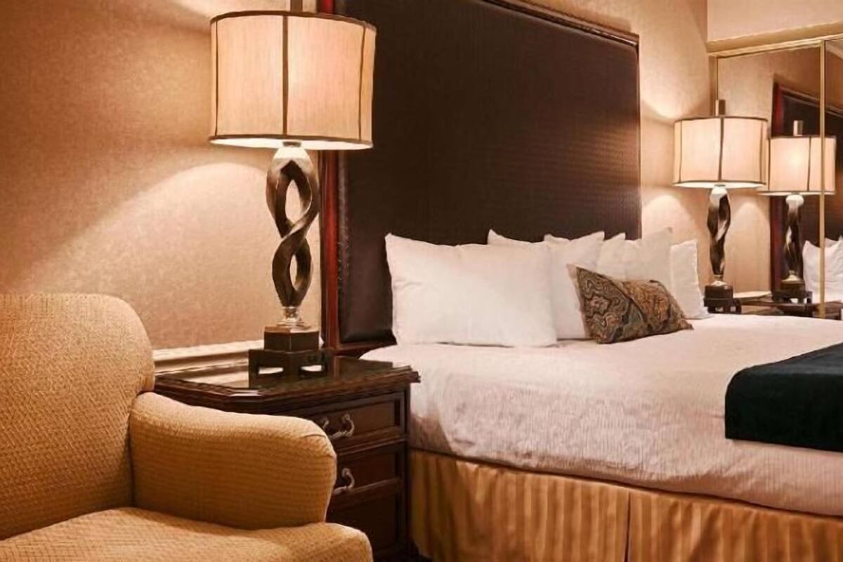 A hotel room with a bed, a chair, a nightstand with a lamp, and a mirror on the wall.