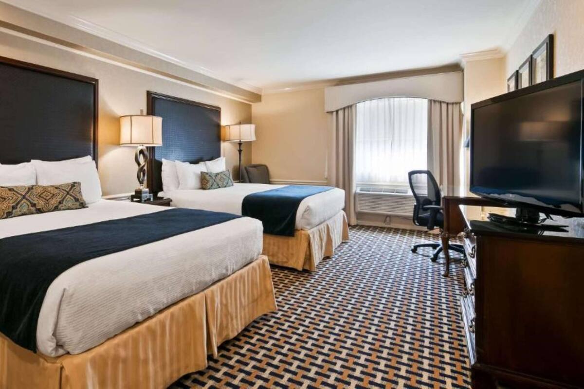 A hotel room with two beds, a desk, a television, and a patterned floor.