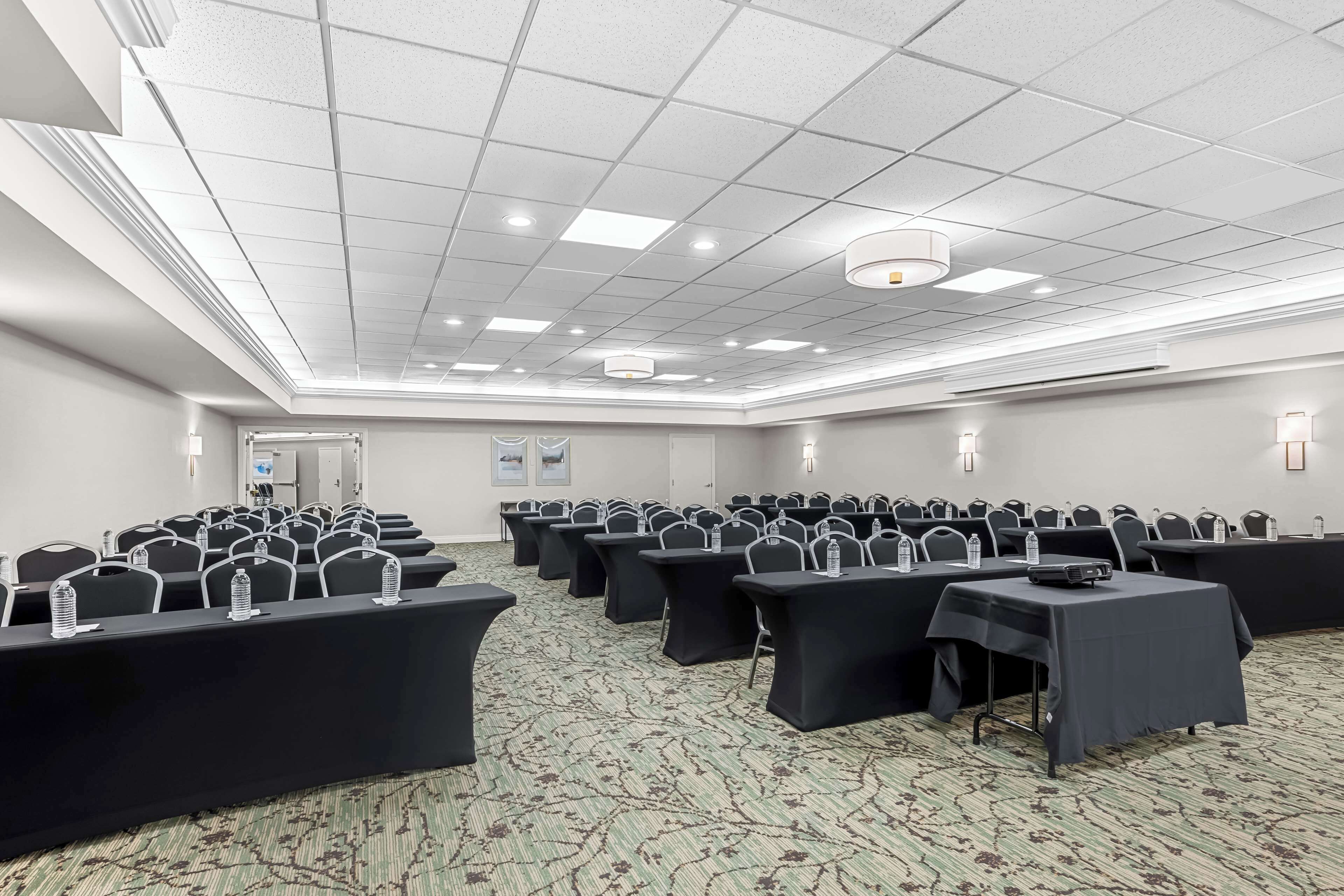A conference room with rows of tables and chairs, a patterned carpet, and a ceiling with recessed lighting.