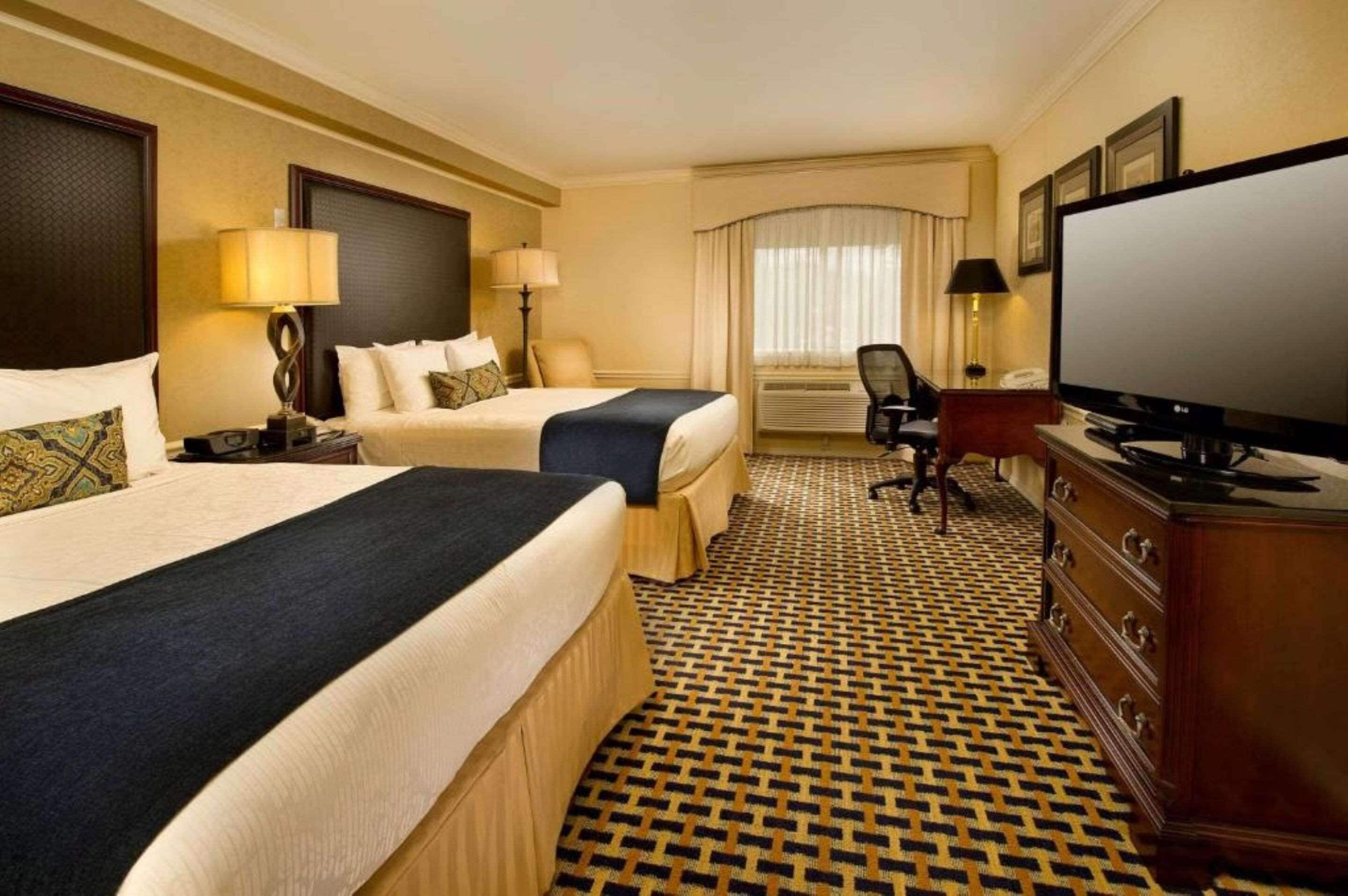 Ein Hotelzimmer mit zwei Betten, einem Fernseher, einem Schreibtisch und einem gemusterten Teppich.