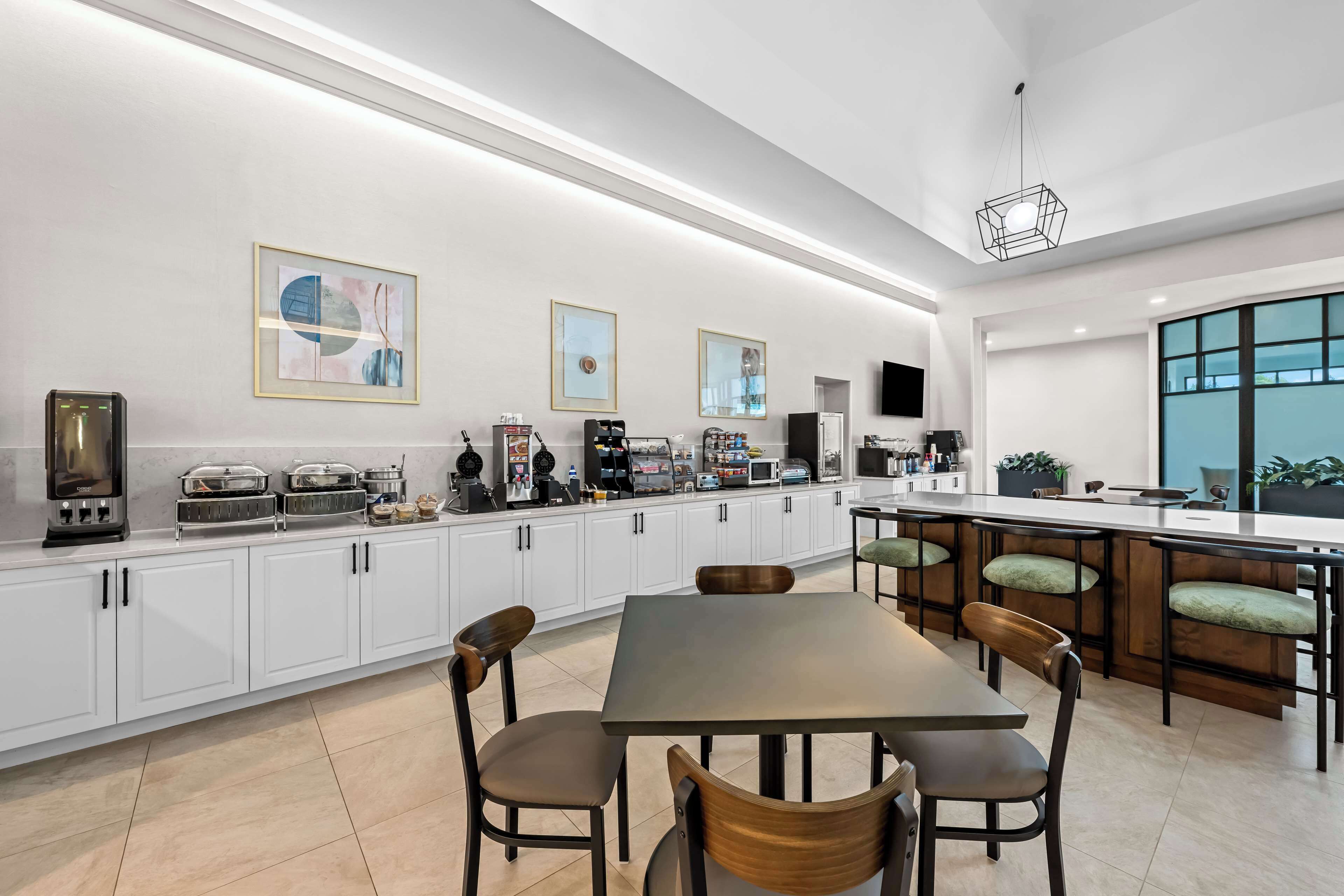 A modern kitchen with white cabinets, a dining area with a dark table and wooden chairs, and a bar area with stools.