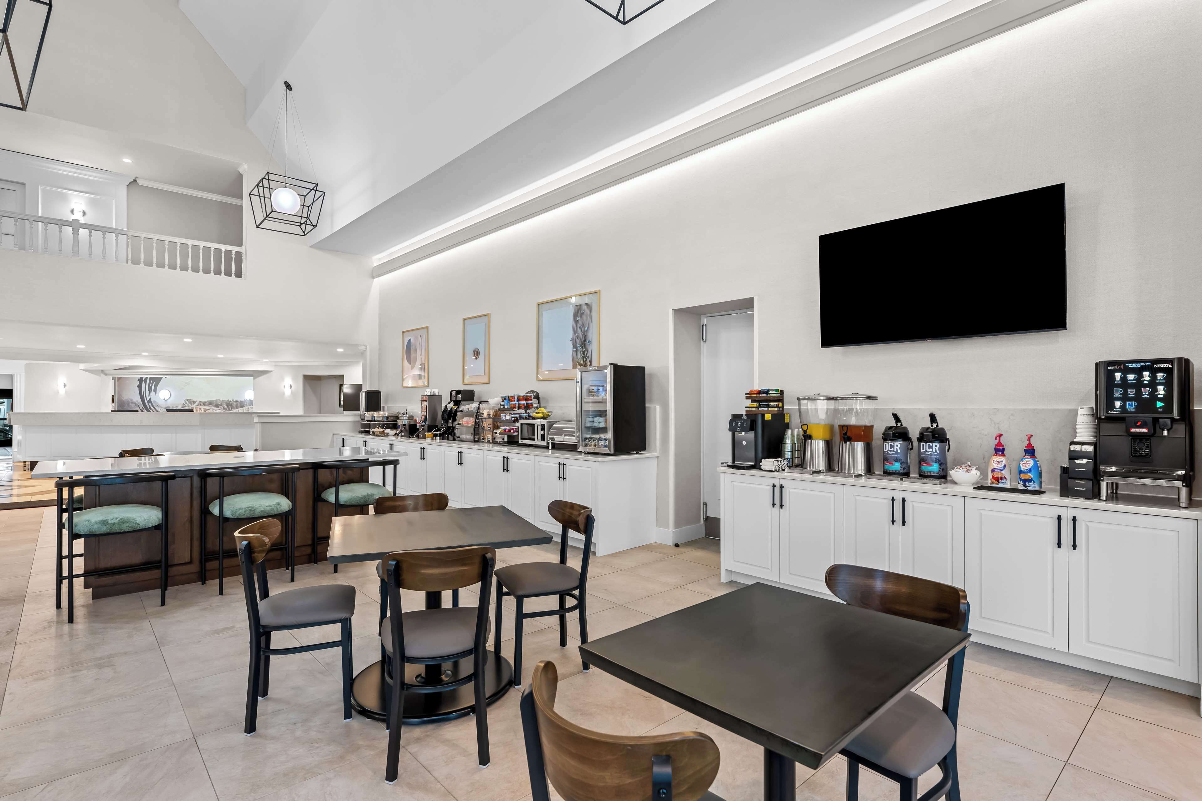 A spacious kitchen with a high ceiling, a dining area with wooden chairs, and a large flat-screen TV mounted on the wall.
