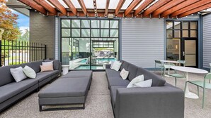 Un patio exterior con una pérgola de madera, sofás grises y vista a la piscina.