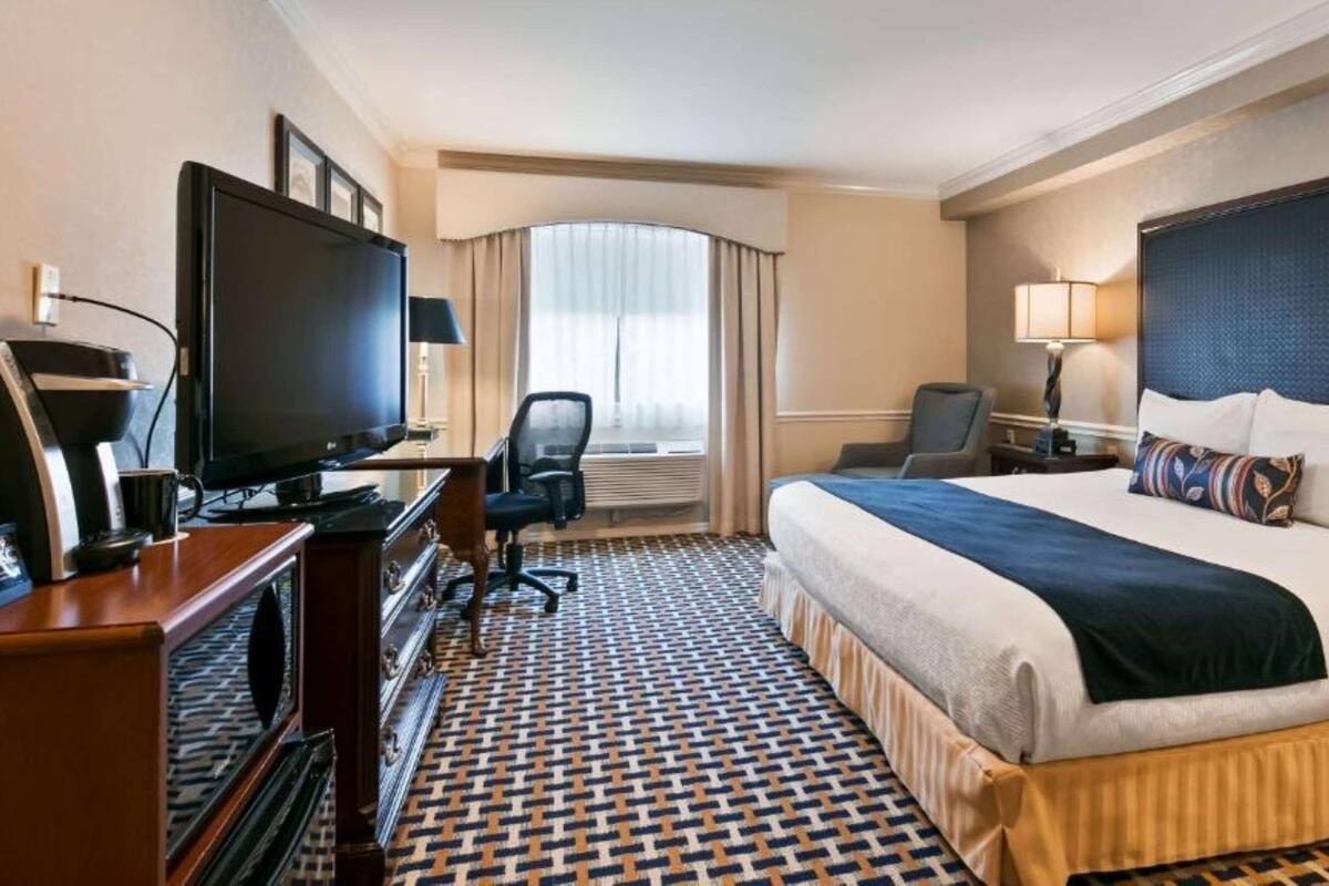 A hotel room with a large bed, a desk with a television, a chair, and a window with curtains.