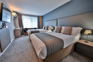 A hotel room with two beds, a TV mounted on the wall, a desk with a chair, and a window with curtains. - Kensington Court Hotel (London)