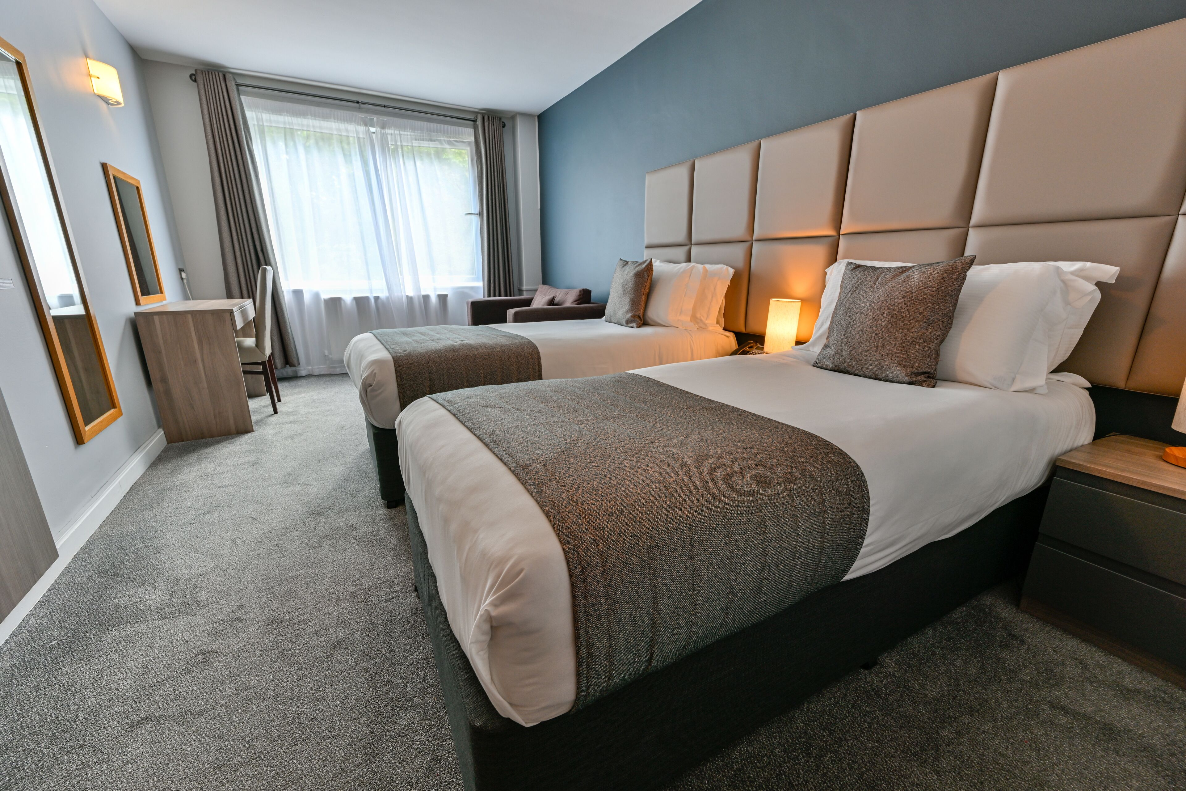A hotel room with two beds, a desk, and a chair.