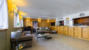 A modern living room with a sofa, armchairs, a coffee table, and a glass table with a lamp. There is a kitchen area with wooden cabinets and a refrigerator. - Kensington Court Hotel (London)