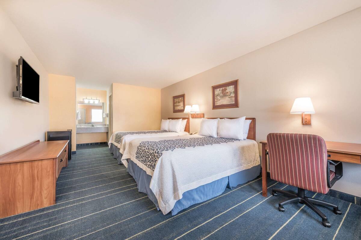 A hotel room with two beds, a desk, a chair, a TV, and a bathroom in the background.