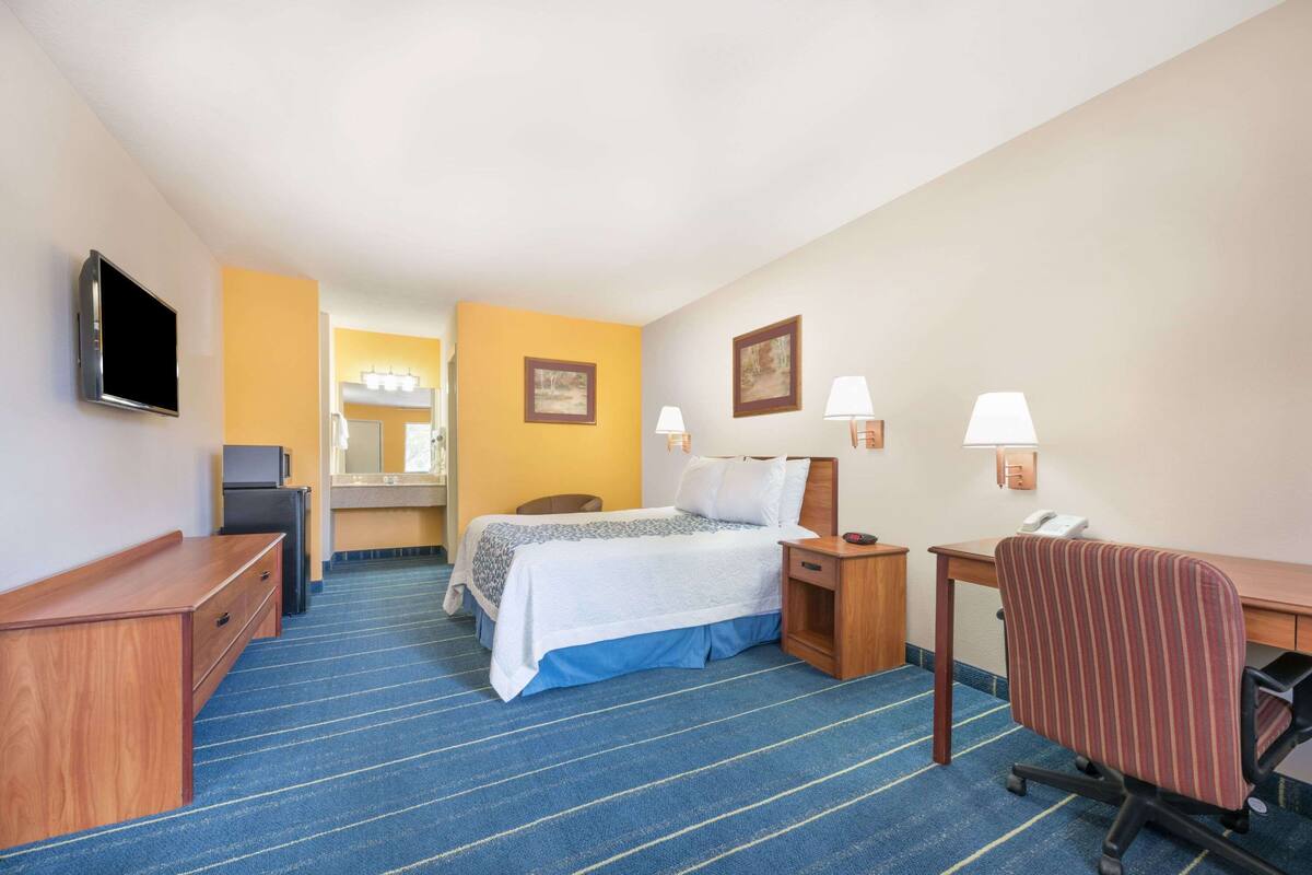 A hotel room with a bed, desk, chair, TV, and a small kitchenette.
