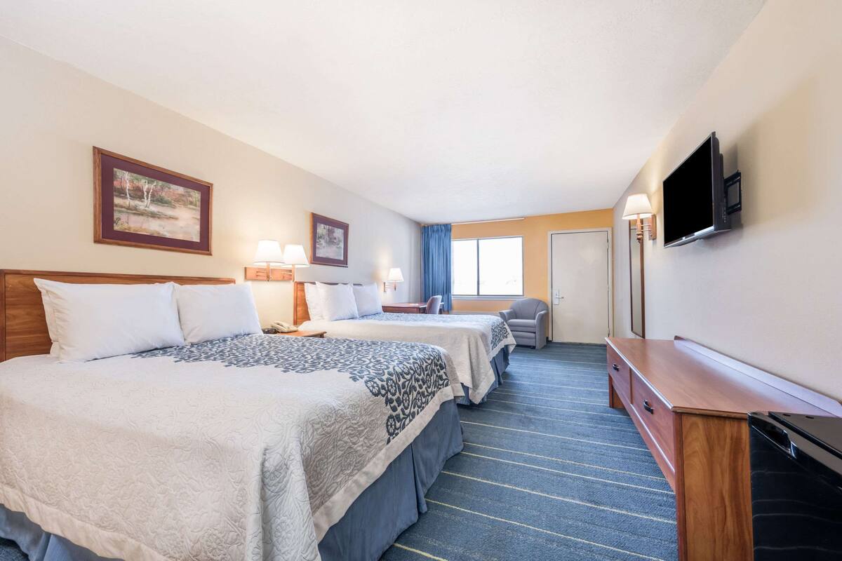 A hotel room with two beds, a desk, a television, and a window with curtains.