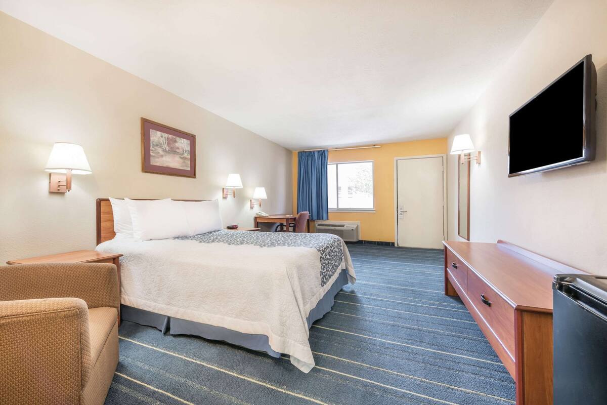 A hotel room with a bed, a desk, a chair, a television, and a wardrobe.
