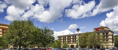A parking lot with several cars, a building with 'ibis hotel' signage, and a clear blue sky with clouds.