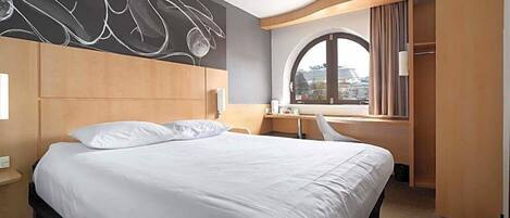 Ein Hotelzimmer mit einem großen Bett, einem Schreibtisch und einem Kleiderschrank.