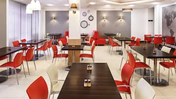 A spacious dining area with multiple tables and chairs, featuring a mix of red and white seating, and a modern ceiling design with integrated lighting.