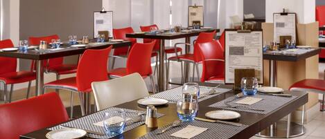 A restaurant with red chairs and tables, each set with plates, cutlery, and glasses.