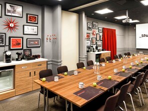 Ein Konferenzraum mit einem langen Tisch, Stühlen, einer Projektionsleinwand und gerahmten Bildern an den Wänden.