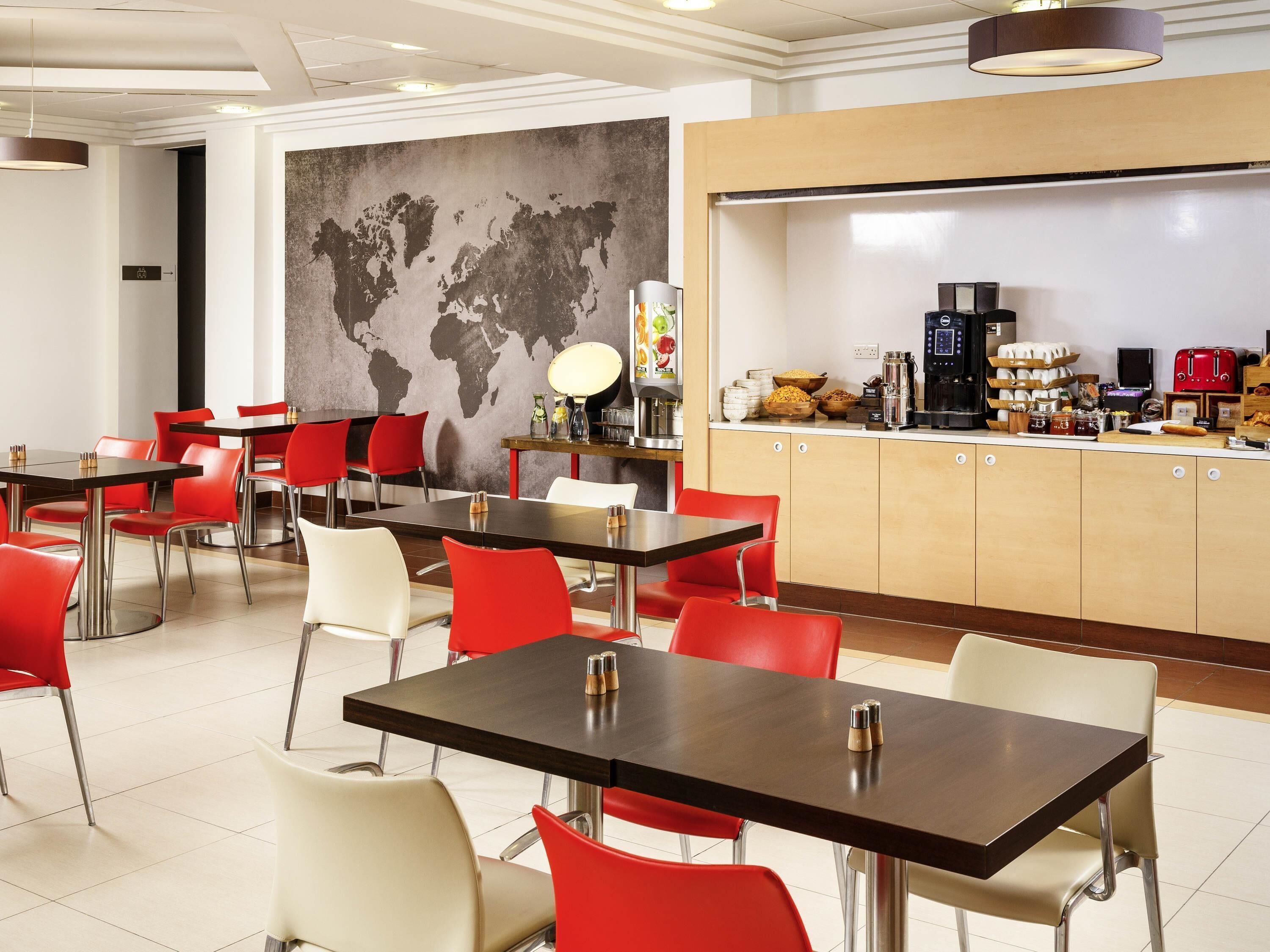 Un comedor moderno con mesas y sillas, un mapa del mundo en la pared y una barra de desayuno con diversos alimentos.