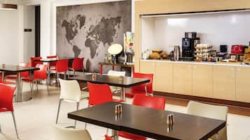 Un comedor moderno con mesas y sillas, un mapa del mundo en la pared y una barra de desayuno con diversos alimentos.