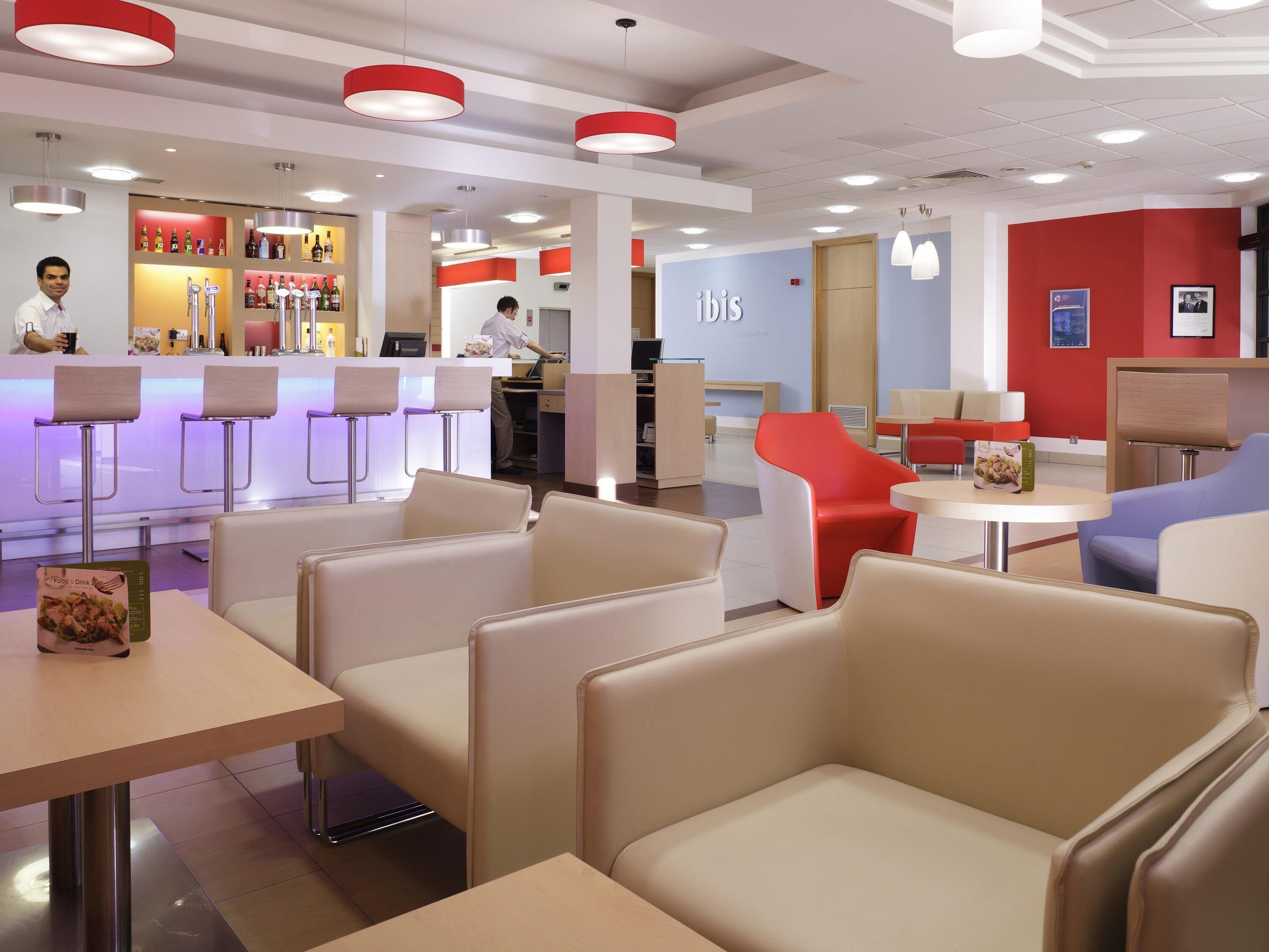 A modern interior with bar seating, a reception area, and a seating area with tables and chairs.