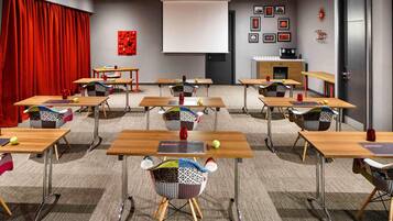 Un salón de conferencias con mesas, sillas, una pantalla de proyector y una cortina roja.
