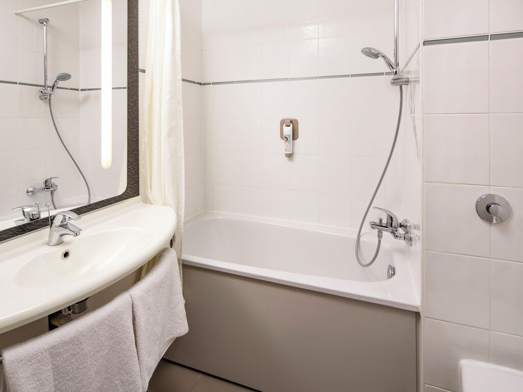 Une salle de bain avec un lavabo blanc, un miroir, une baignoire et une douche.