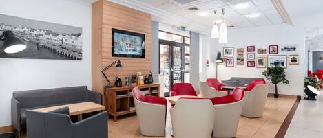 A modern interior with a reception desk, red and grey seating, a TV, and framed pictures on the wall.