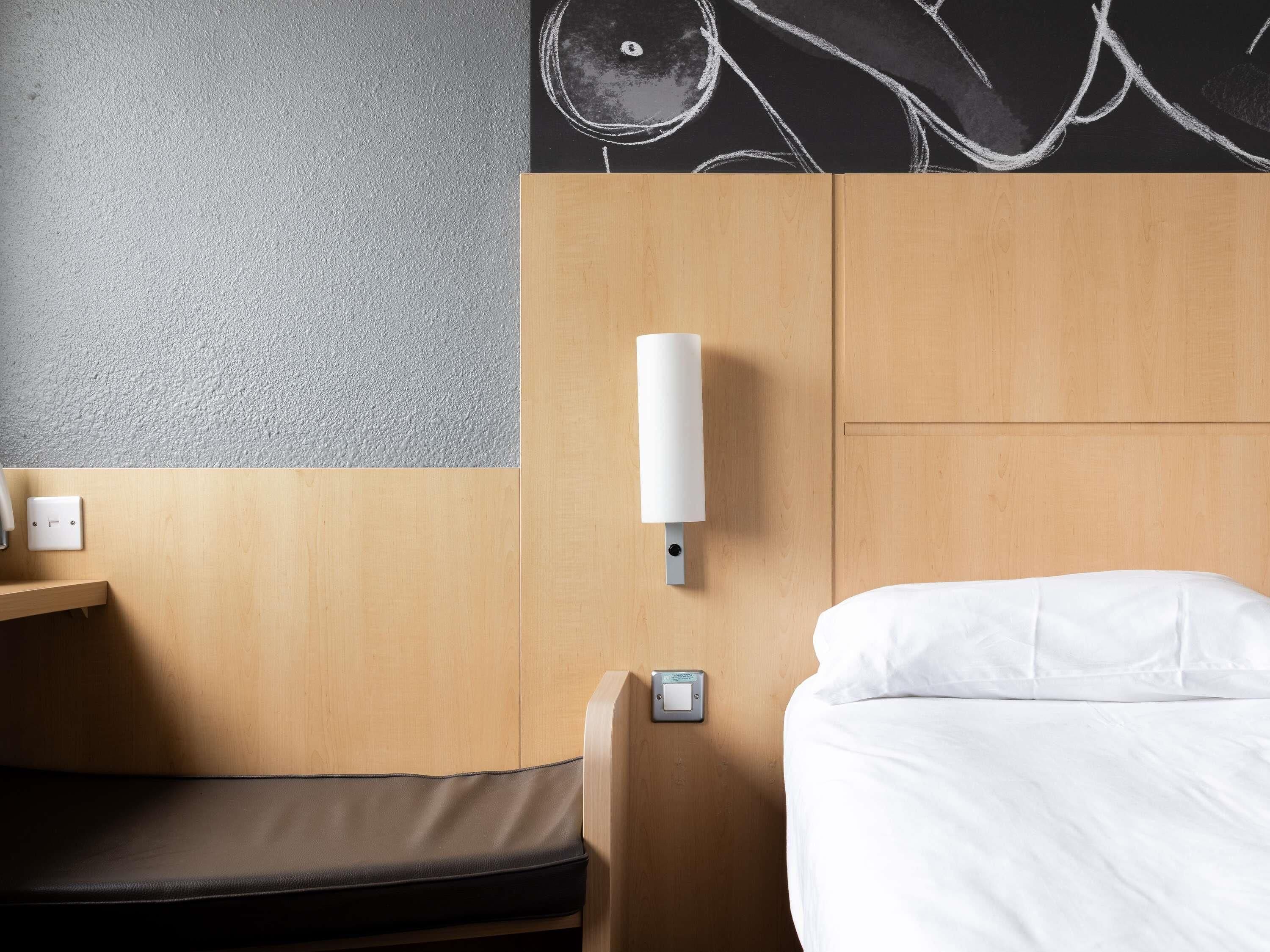 Een hotelkamer met een bed, nachtkastje, een wandlamp en een stopcontact.
