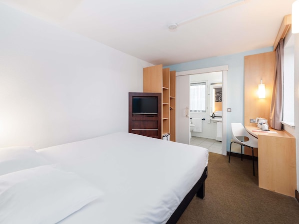 A hotel room with a bed, a TV, a desk with a chair, and a bathroom visible through an open door. - ibis Southampton Centre (Southampton)