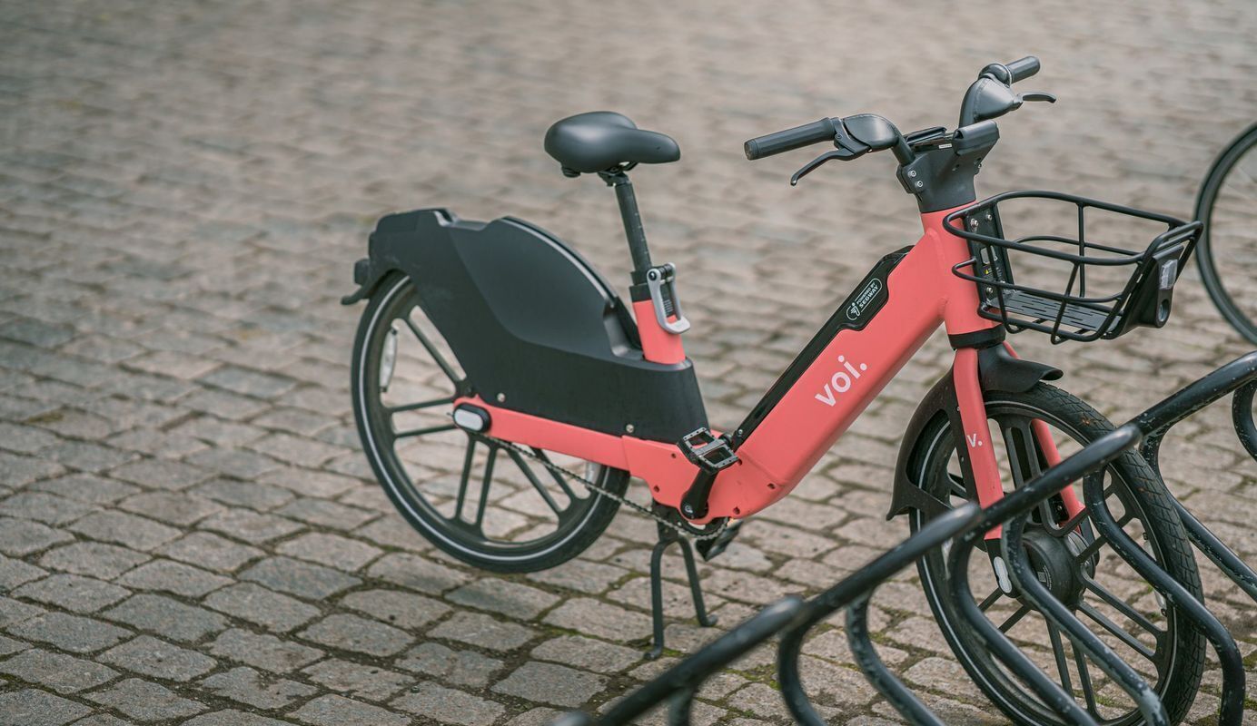 A red and black electric bicycle with a basket, parked on a cobblestone surface.
