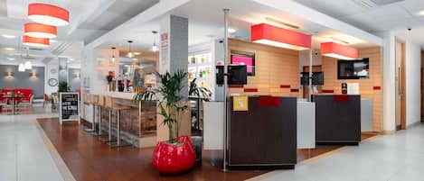 A modern hotel lobby with a reception desk, seating area, and a bar.