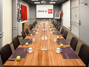 A conference room with a long table, chairs, and a projector screen displaying 'SPACE BY ibis HOTELS'.