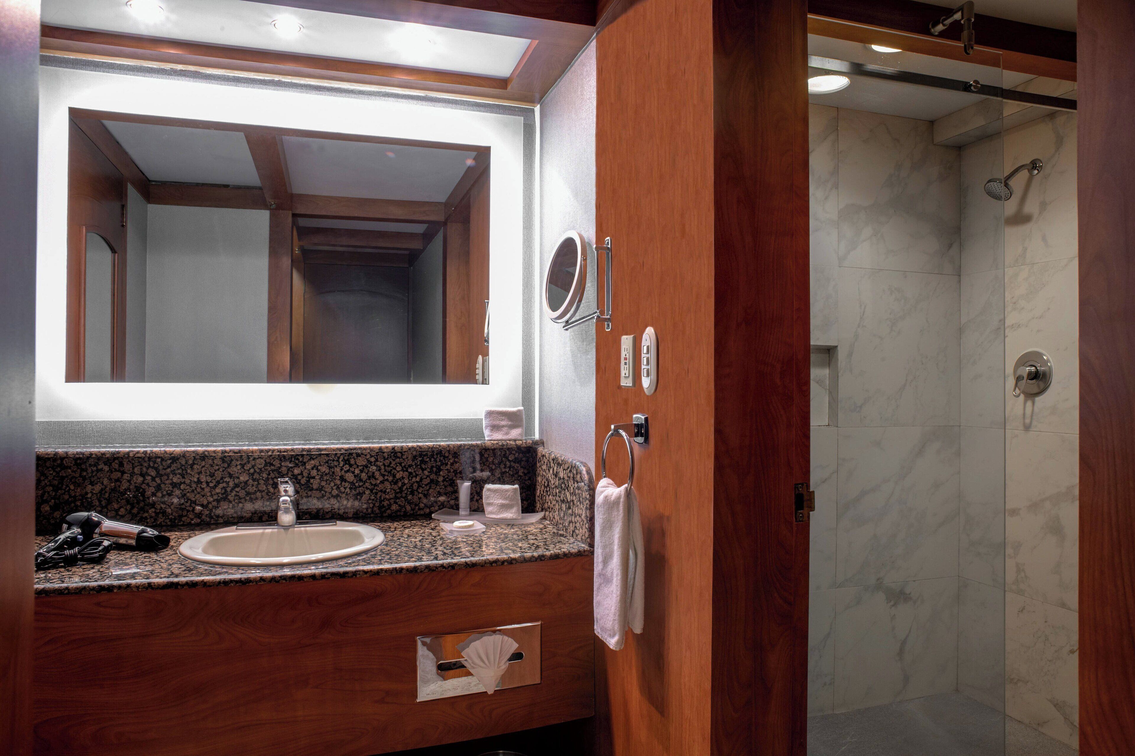 A bathroom with a wooden vanity, a large mirror, a sink, and a shower area.