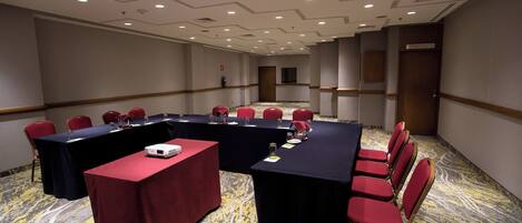 A conference room with a long table, red chairs, and a projector.
