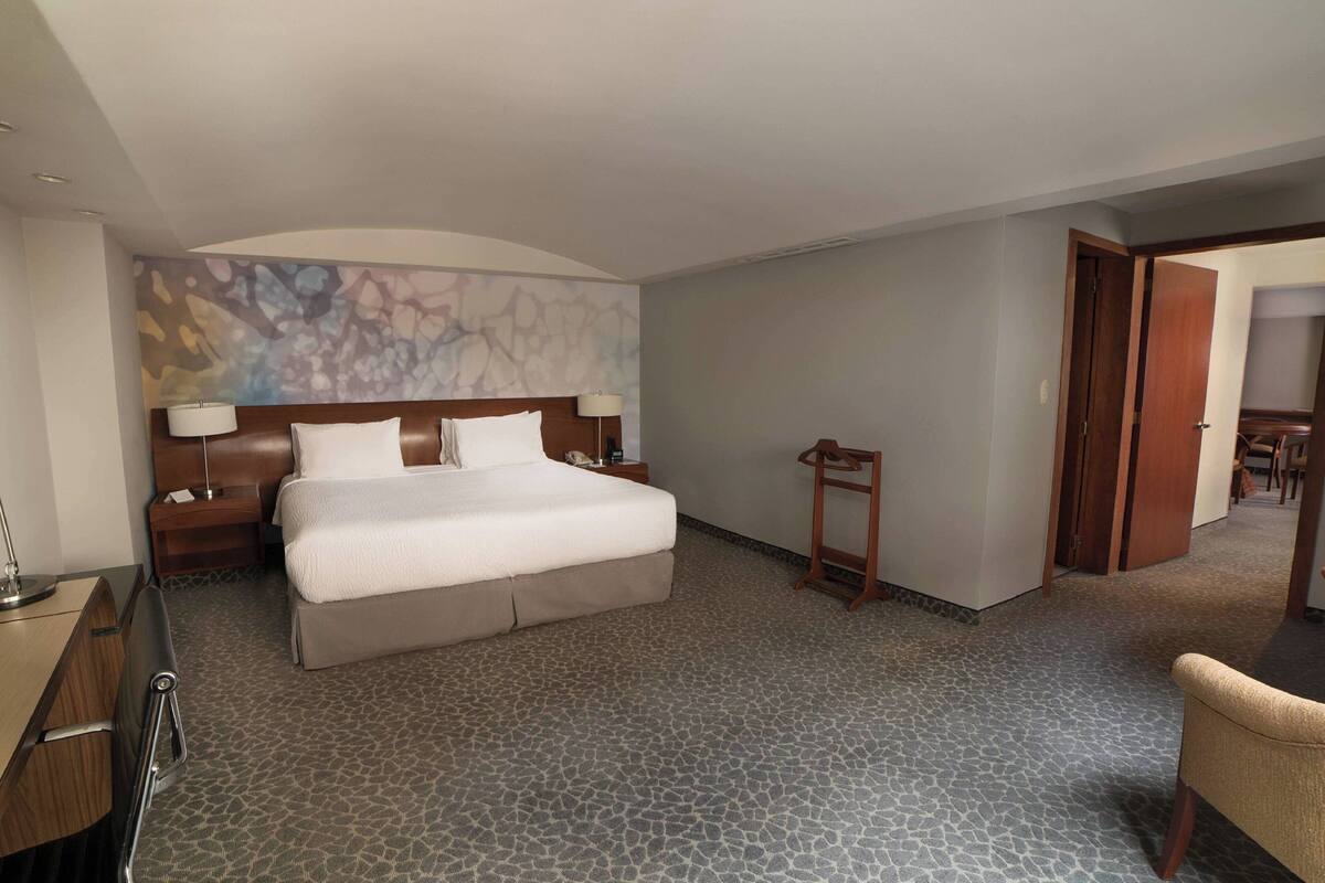 Habitación de hotel con una cama grande, un escritorio, una silla, una mesita de noche y una pared con diseño texturizado.