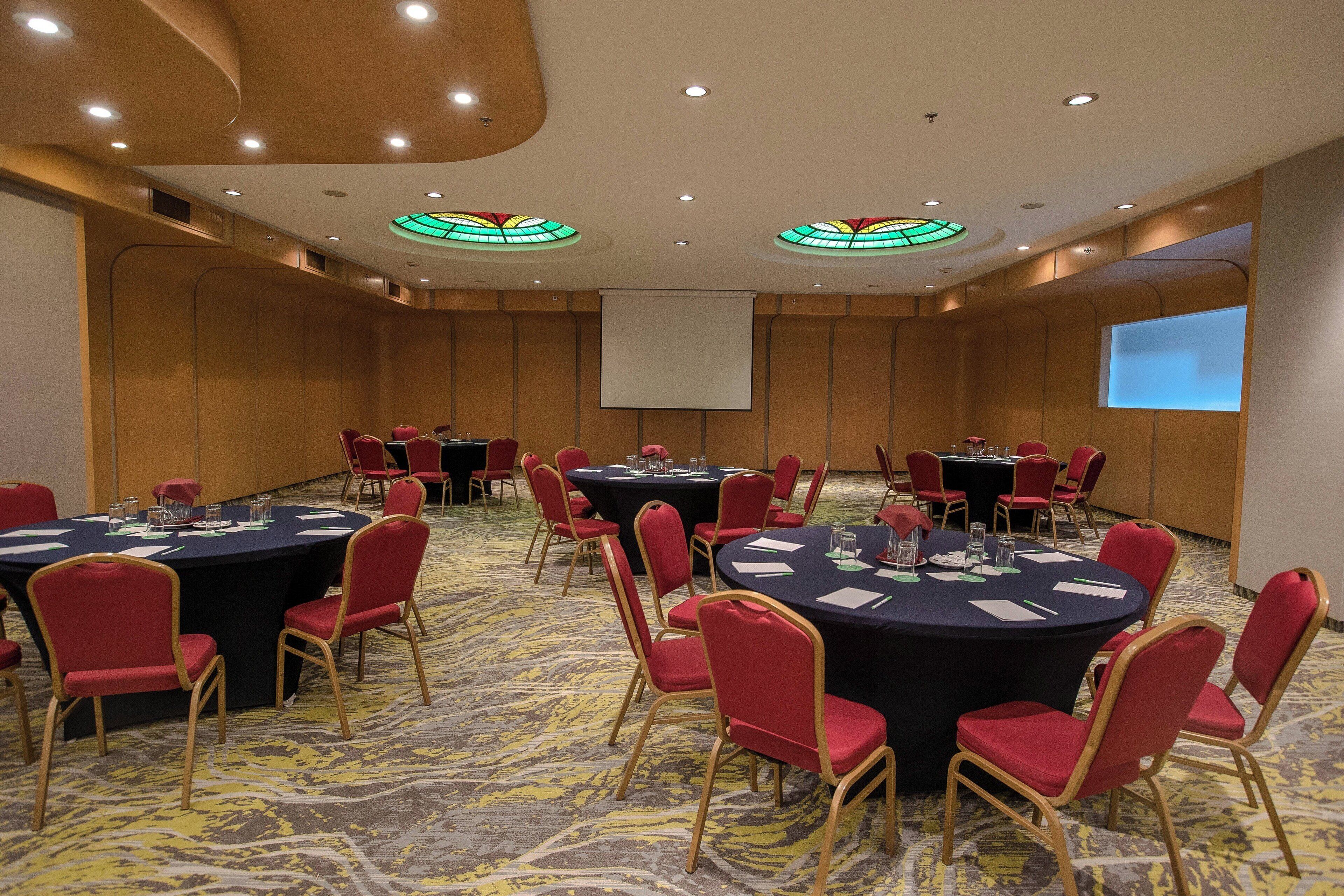 A conference room with round tables, red chairs, and a projector screen.